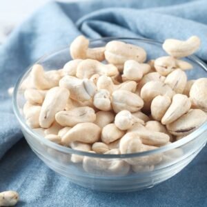 Home A glass bowl filled with raw cashews on a blue cloth, perfect for healthy snacking.